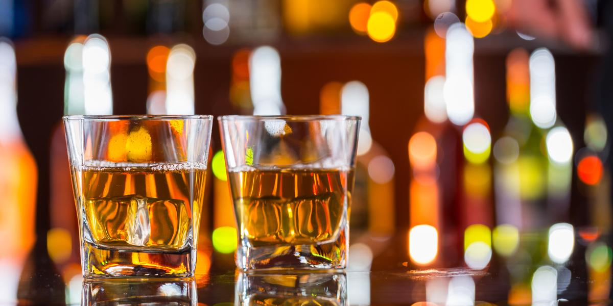 Two glasses of whiskey on the rocks on a reflective bar top